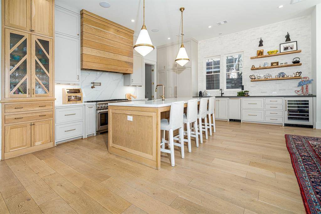 Modern kitchen features light wood floors, a large island with seating, sleek countertops, and stylish backsplash.