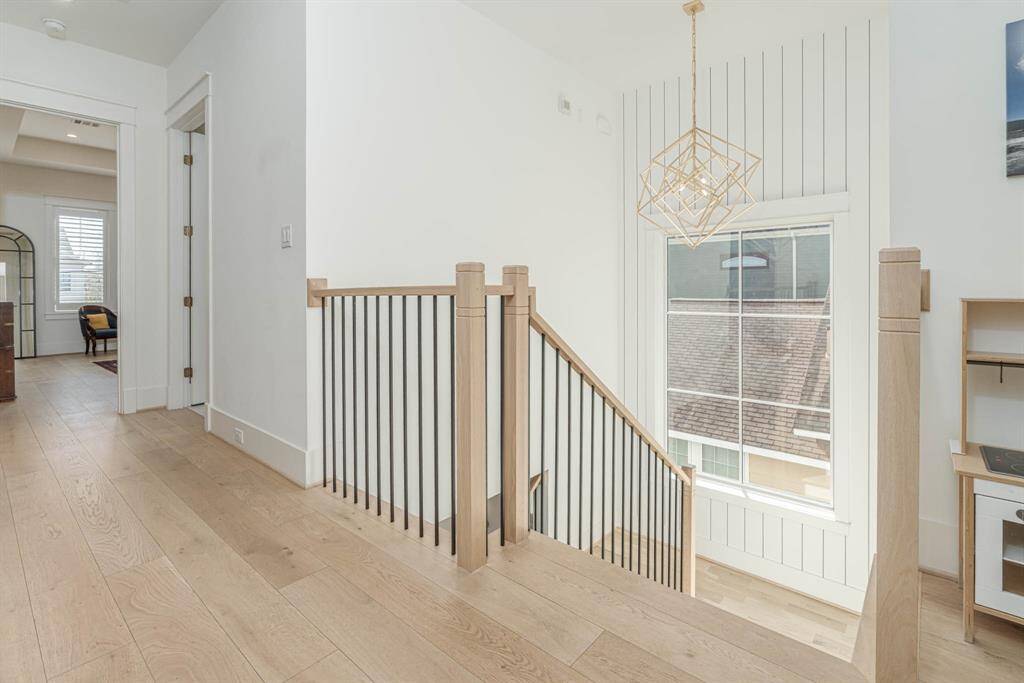 bright, modern hallway with light wood flooring and a staircase featuring sleek black balusters. A large window allows natural light to fill in