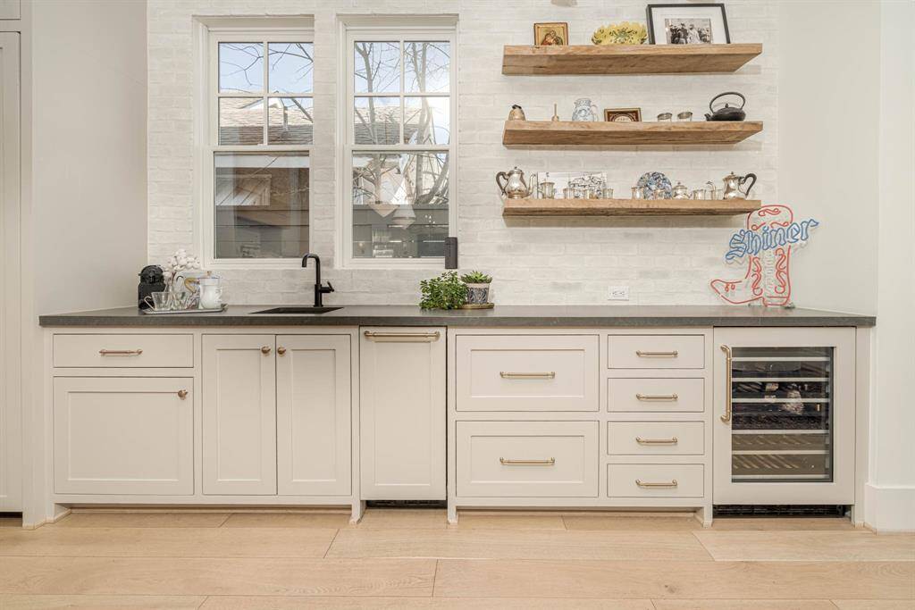 More counter space with wine cooler, open shelving with decorative items, and a stylish black sink. The space is brightened by two large windows.