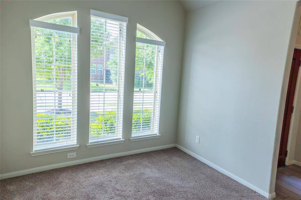 Bright room with three large arched windows and neutral walls, offering plenty of natural light and a cozy carpeted floor. Ideal for a home office or reading nook.