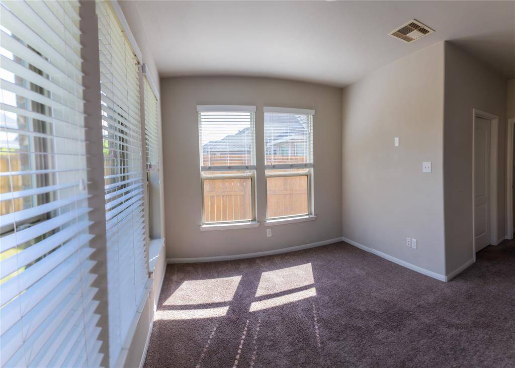 This room features large windows with blinds, offering plenty of natural light and a view of the fenced backyard. The carpeted floor adds warmth, and there's a neutral color scheme that provides a blank canvas for personalization.