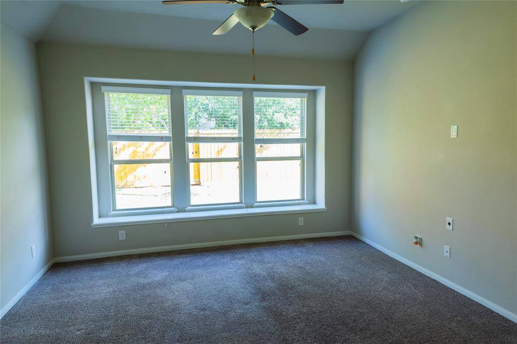 Bright, spacious room with large windows offering plenty of natural light, neutral walls, and a ceiling fan. Ideal for a cozy living area or bedroom.