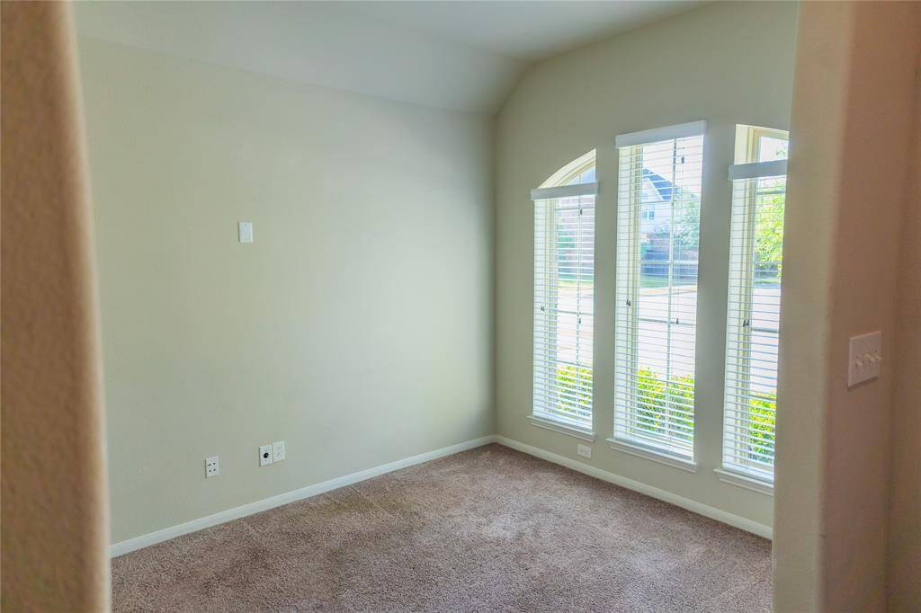 This room features a cozy carpeted floor and large arched windows with blinds, offering plenty of natural light. Ideal for a small office or reading nook.