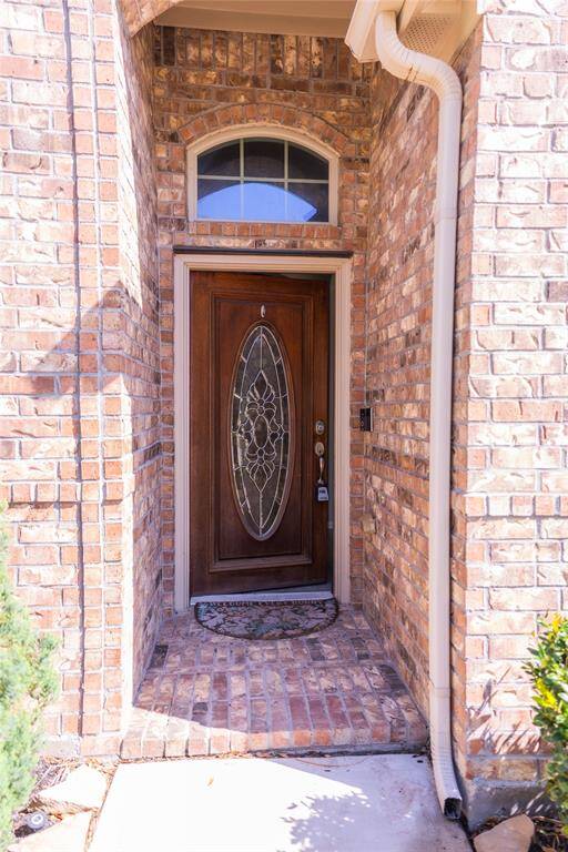 This photo showcases a welcoming front entrance with a wooden door featuring an elegant oval glass design. The entryway is framed by a brick exterior, offering a classic and inviting look.