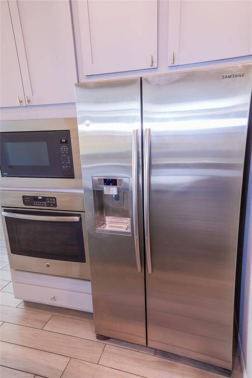 This photo showcases a modern kitchen setup featuring stainless steel appliances, including a side-by-side refrigerator with a water dispenser, built-in microwave, and oven. The cabinetry is sleek and contemporary, complementing the tiled flooring.