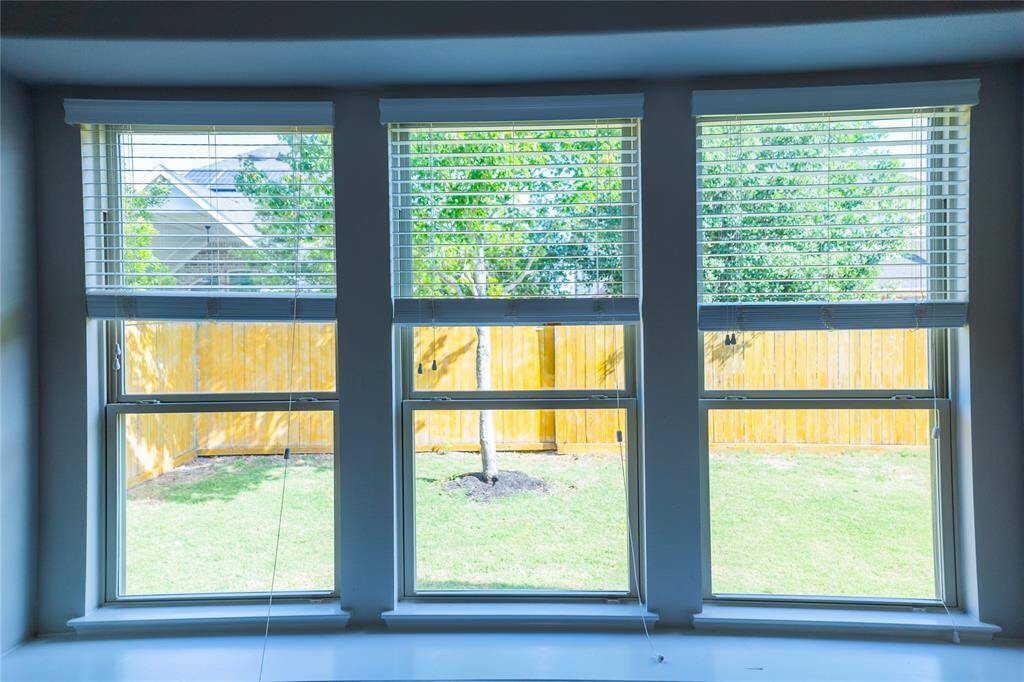 This photo showcases a set of large windows with blinds, offering a view of a well-maintained backyard with a wooden fence and trees, providing ample natural light.