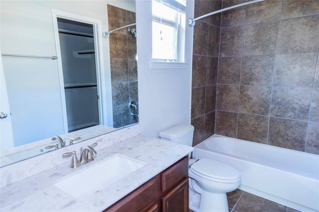 This bathroom features a modern design with a sleek vanity and marble countertop, a bathtub with tiled walls, and a window for natural light.
