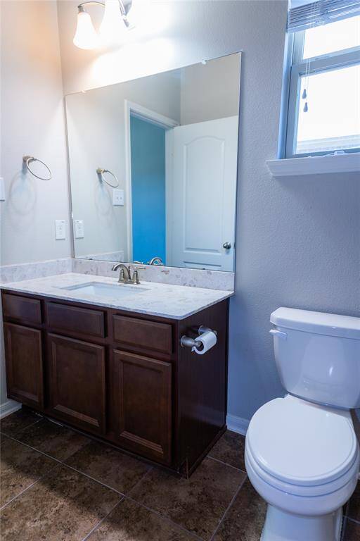 Bright and clean bathroom with a modern vanity, marble countertop, large mirror, and a window for natural light. Features a toilet, tile flooring, and elegant lighting.