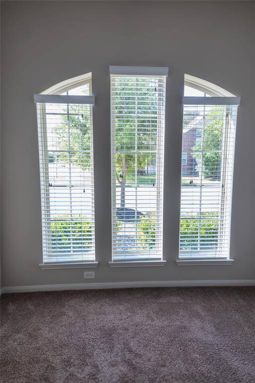Bright room with large arched windows, offering plenty of natural light and a view of the street. Carpeted floor adds warmth and comfort.