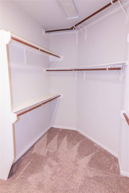 This photo shows a spacious walk-in closet with multiple shelves and rods for ample storage. The closet is carpeted and has a light fixture for visibility.