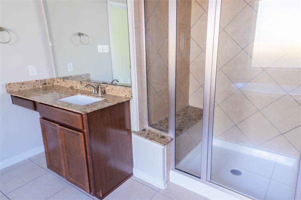 This bathroom features a modern glass-enclosed shower with beige tiling and a sleek vanity with a granite countertop and dark wood cabinet, offering a clean and contemporary look.