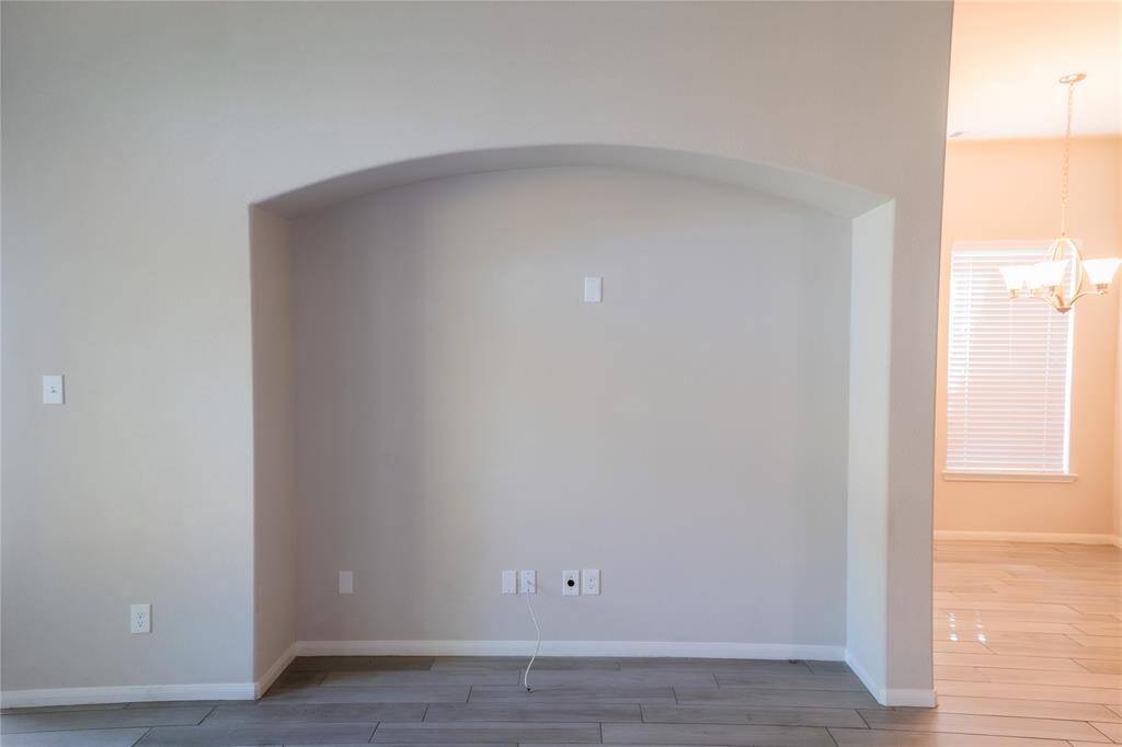 This photo shows a room with a recessed wall niche, ideal for a media center, featuring outlets and cable connections. The space has tiled flooring and an adjacent well-lit dining area with a window and chandelier.