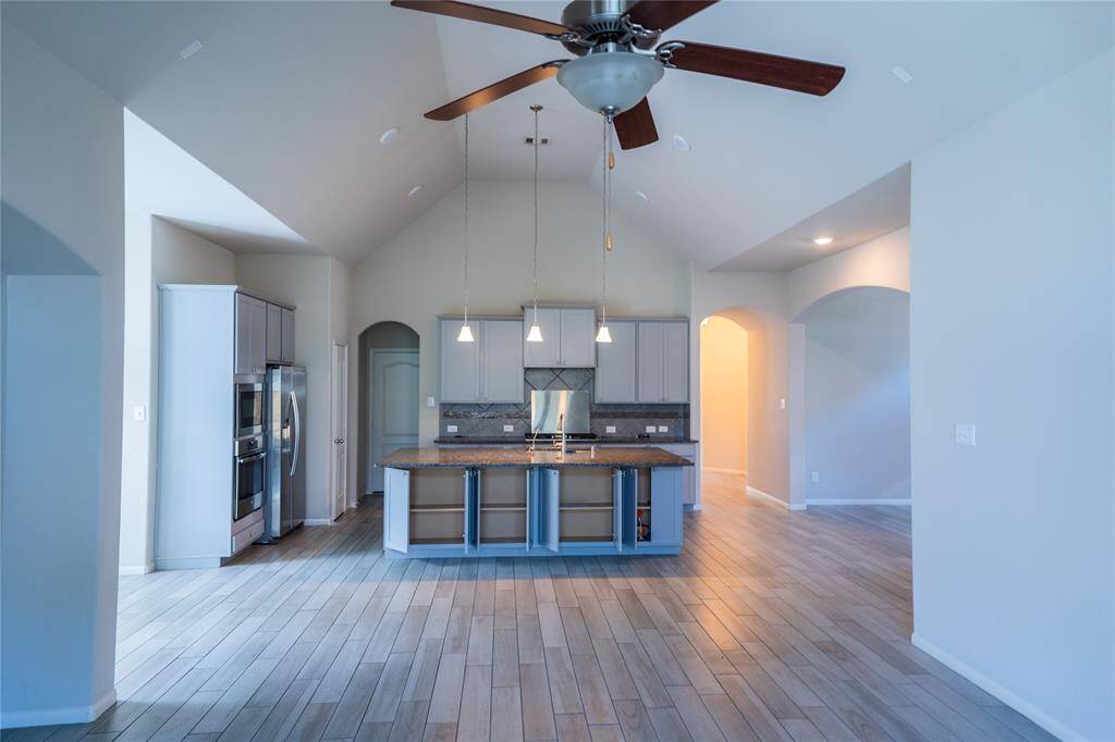 Open-concept kitchen with modern appliances, pendant lighting, and a central island. The light wood flooring and vaulted ceiling with a fan provide a spacious and airy feel.