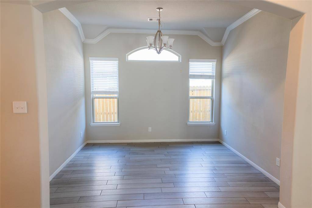 Bright dining room with neutral walls, wood-look tile flooring, and a stylish chandelier. Features two large windows and a smaller arched window for natural light.