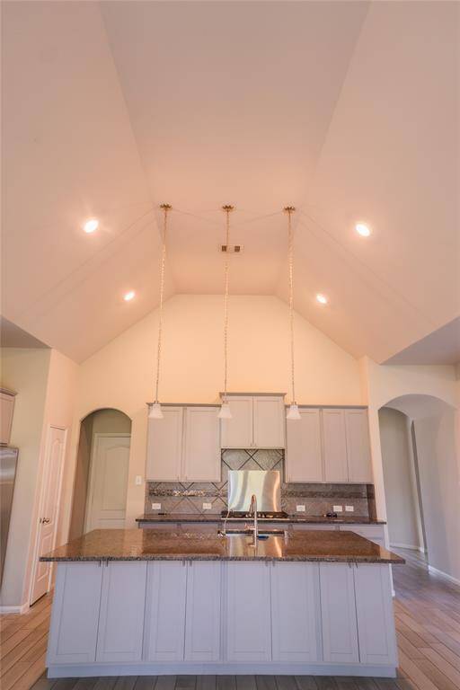 This kitchen features high vaulted ceilings with recessed lighting and modern pendant lights. It includes a large central island with granite countertops, stainless steel appliances, and ample cabinetry, creating a spacious and elegant cooking area.