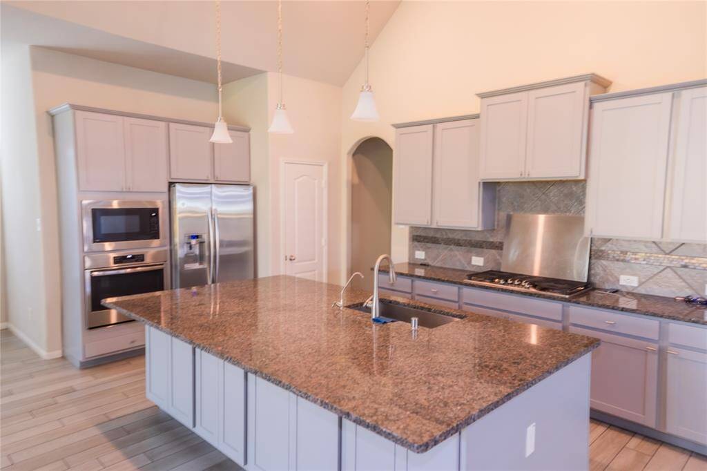 Spacious kitchen with granite countertops, stainless steel appliances, and ample cabinet space. Features a large island with a sink, modern lighting, and a stylish backsplash.