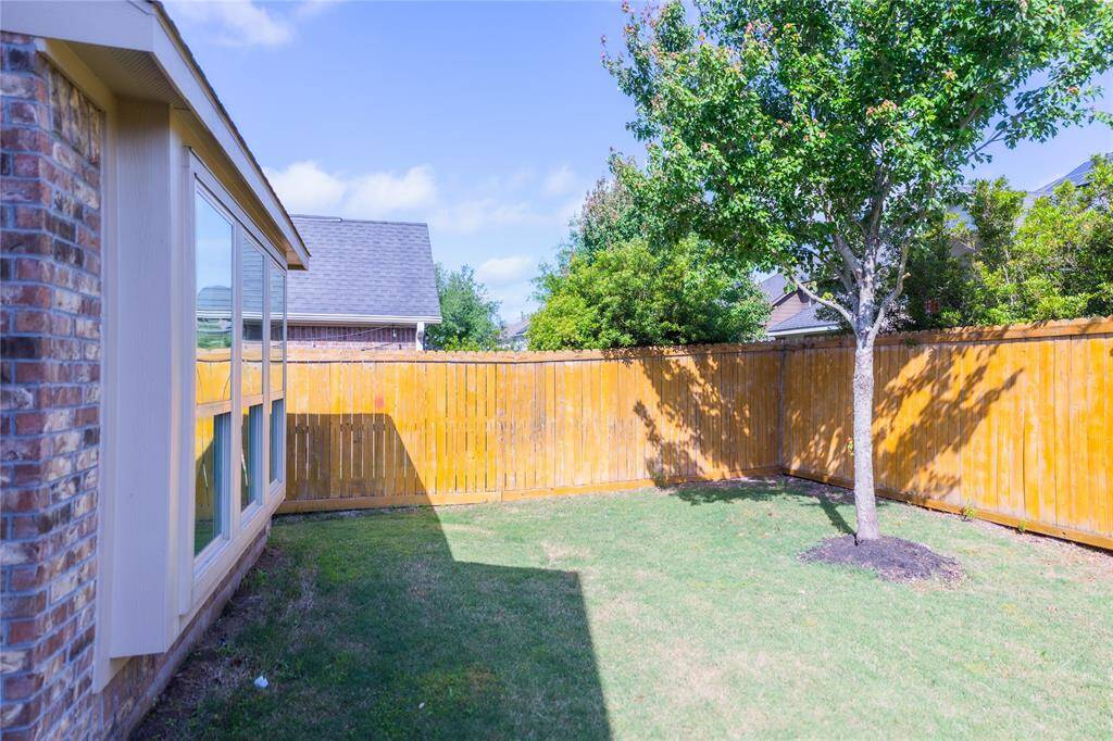 This photo showcases a cozy backyard with a well-maintained lawn, a single tree, and a wooden privacy fence. The brick exterior of the house features large windows that allow natural light to stream in, ideal for a private and serene outdoor space.