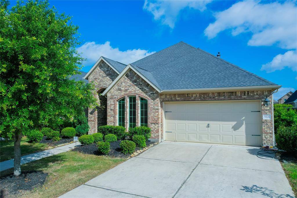 Charming single-story brick home with a well-maintained front yard, featuring lush greenery and a spacious two-car garage. The arched windows add elegance and natural light, while the clean driveway and sidewalk enhance curb appeal.