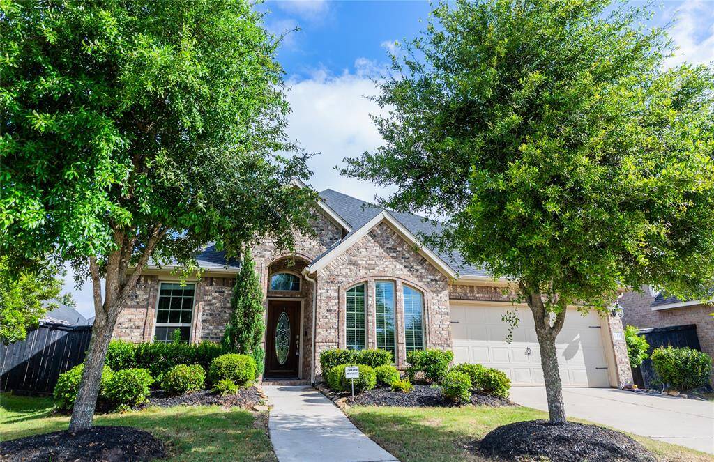 This charming home features a brick exterior with a welcoming arched entrance, complemented by well-maintained landscaping and mature trees. The car garage and large front windows add to its curb appeal.