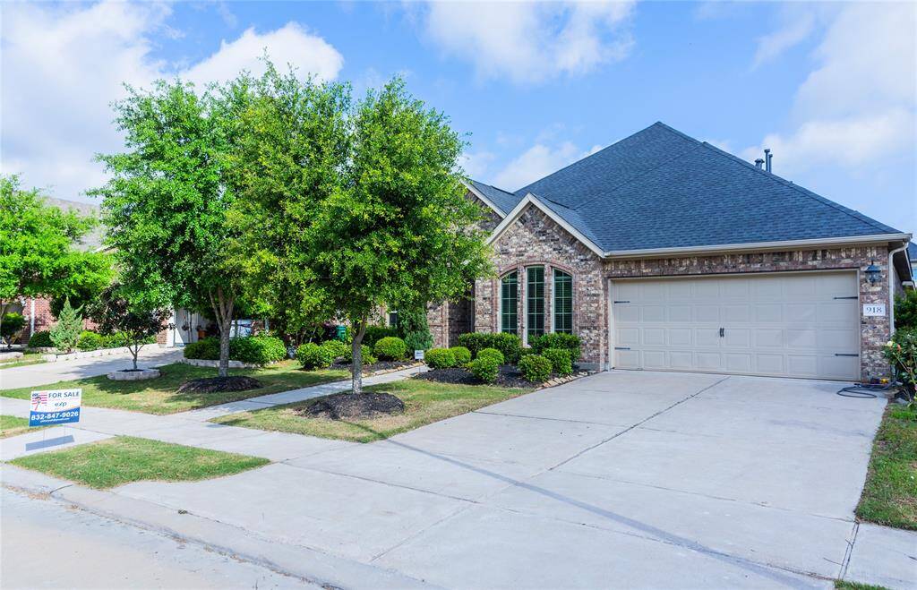 Charming brick home with a car garage, manicured landscaping, and mature trees lining the front. Features a well-maintained driveway and a "For Sale" sign. Ideal for buyers seeking a welcoming and attractive property.