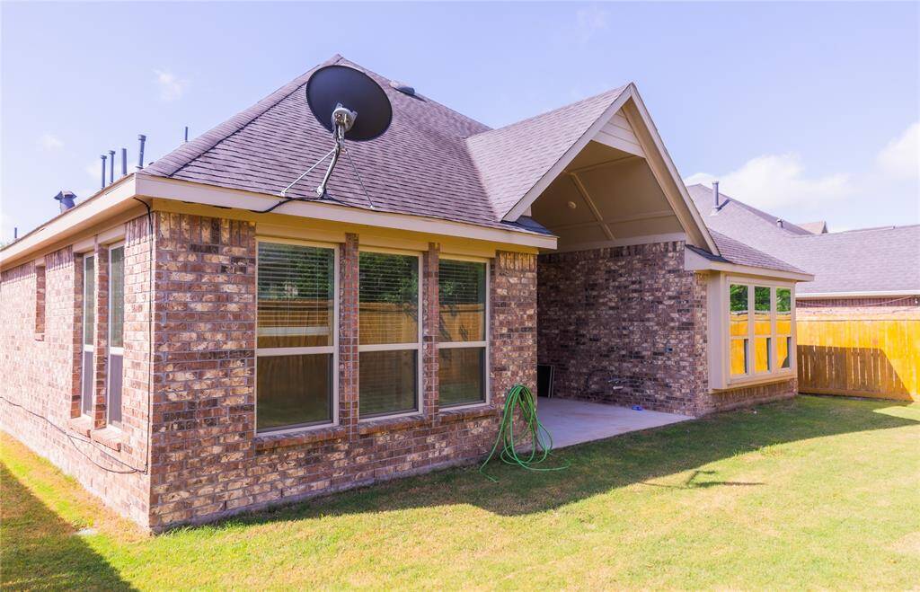 This photo showcases a brick exterior home with a sloped roof, featuring a covered patio and multiple large windows, providing ample natural light. The backyard is grassy and fenced, offering privacy and space for outdoor activities.