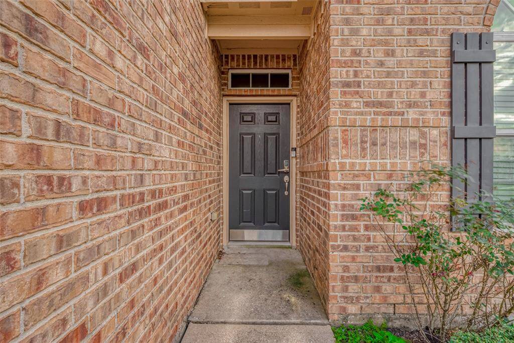 Tucked into a recessed area, the dark wood front door stands out against the warm brick exterior. This covered entrance, framed by brick walls, adds a sense of privacy while offering a stylish contrast to the home’s classic palette.