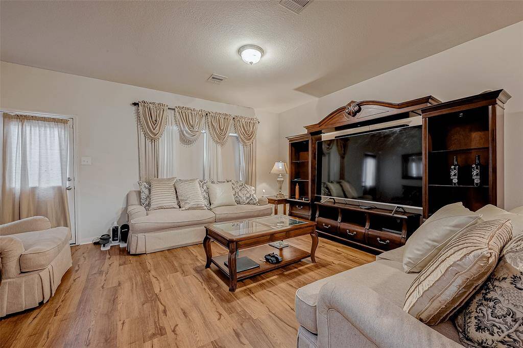 This spacious living area receives natural light from large windows, accentuating the soft neutral walls and wood-like vinyl flooring. With easy access through open walls, the space remains well connected to the kitchen. Stairs to the side lead to the upper level, offering a seamless flow between floors.