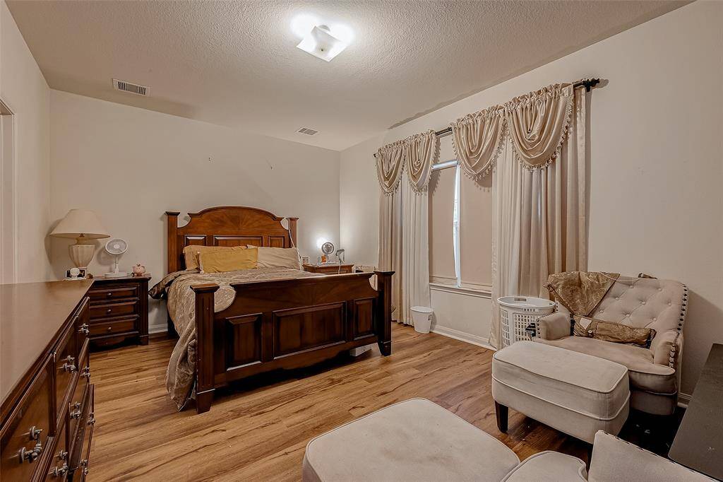 The primary bedroom features large windows that bring in natural light, complemented by warm neutral walls and wood-like vinyl floors. A private en suite bathroom adds convenience and comfort.