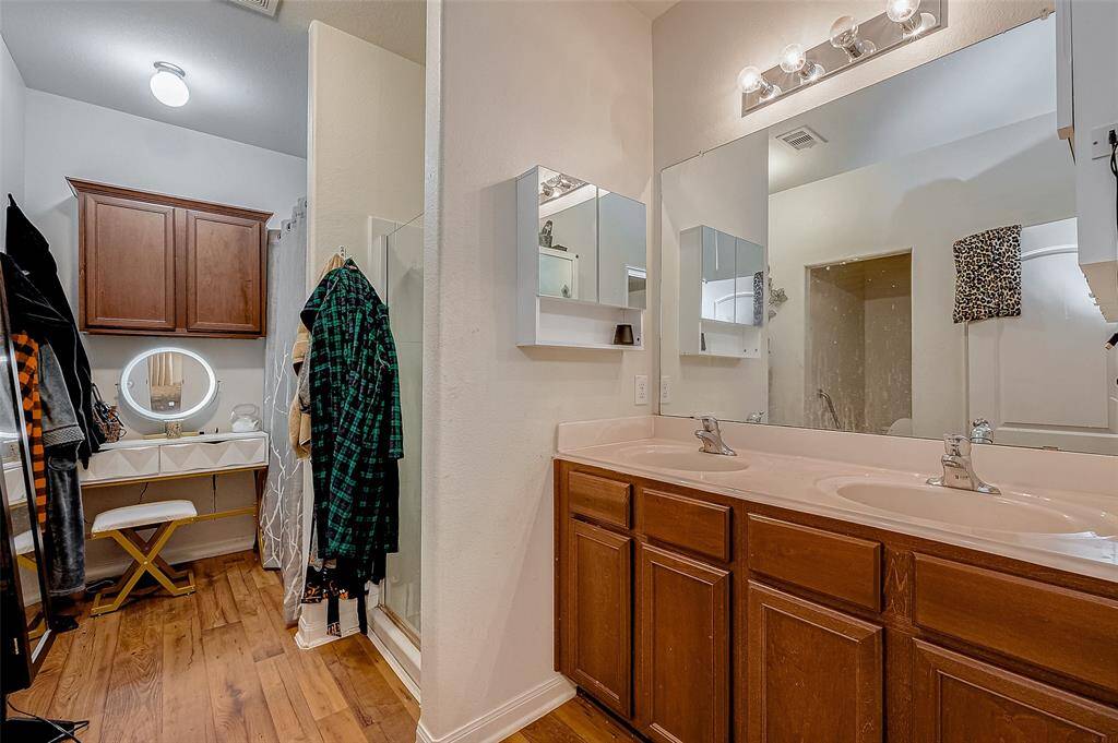 Featuring a dual sink vanity, a large mirror, and plenty of under-cabinet storage, this en suite bath offers both space and efficiency. A separate enclosed shower completes the layout.