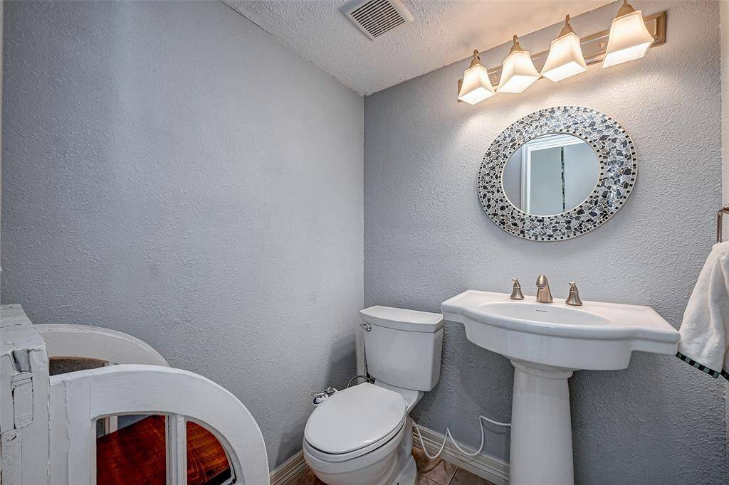 A modern half-bathroom featuring a pedestal sink, a toilet, and a decorative round mirror.
