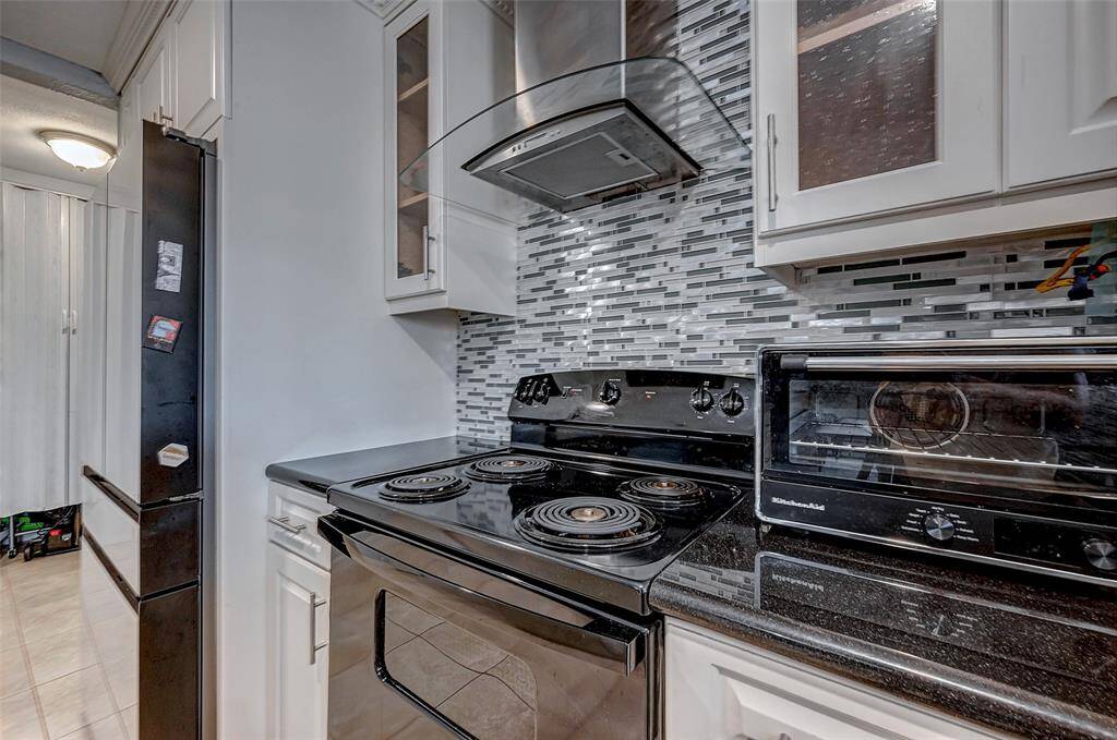 This kitchen features sleek black appliances, including an electric stove, complemented by a modern glass tile backsplash. White cabinetry with glass inserts adds an airy touch, while the dark countertops provide a stylish contrast.