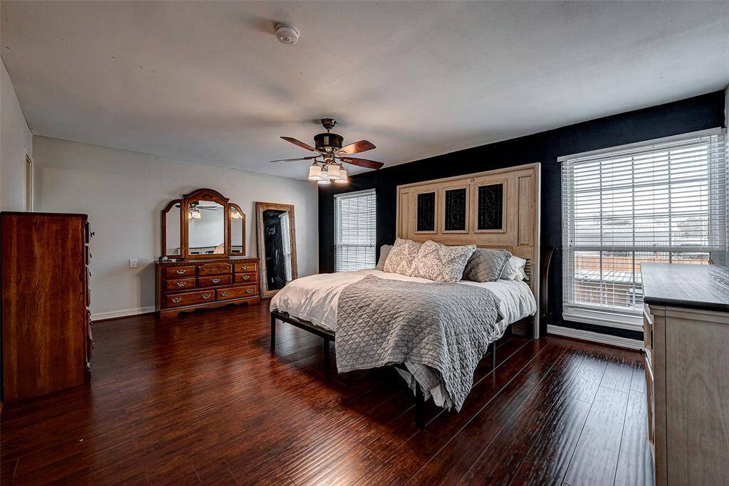 Spacious bedroom with rich hardwood floors, and large windows allowing ample natural light. A ceiling fan adds comfort and style.