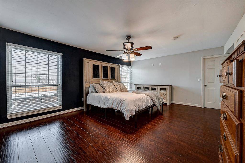 Spacious bedroom with hardwood floors, featuring a large window that lets in natural light. It includes a ceiling fan, dark accent wall, and ample space for furniture.