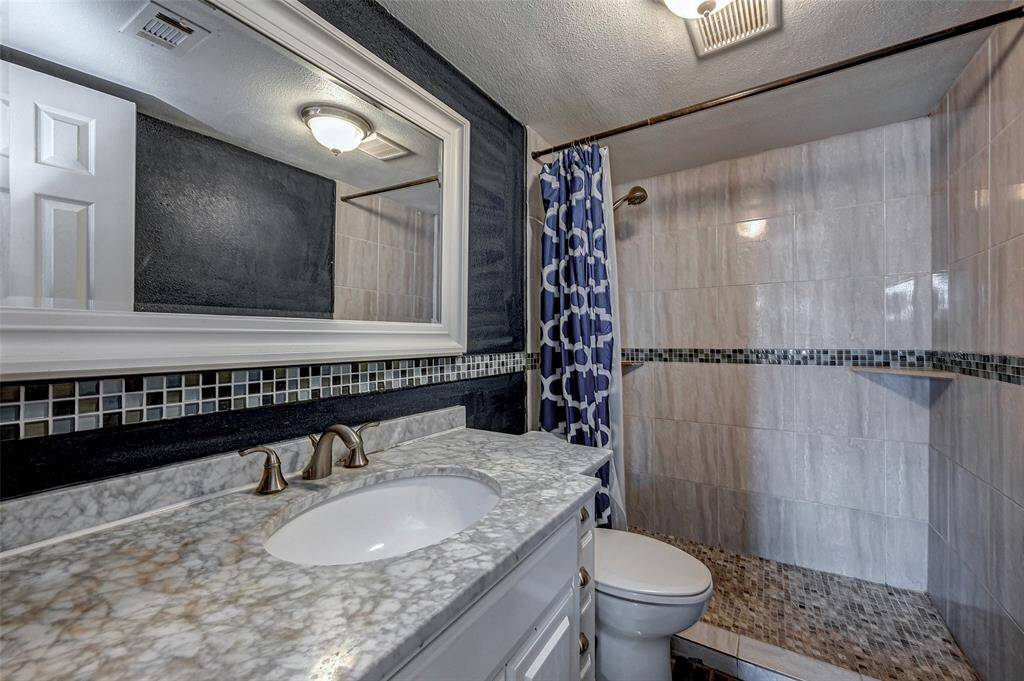 This bathroom features a modern design with a large mirror, stylish marble countertop, and a walk-in shower with mosaic tile accents. The dark wall adds contrast, enhancing the contemporary feel.
