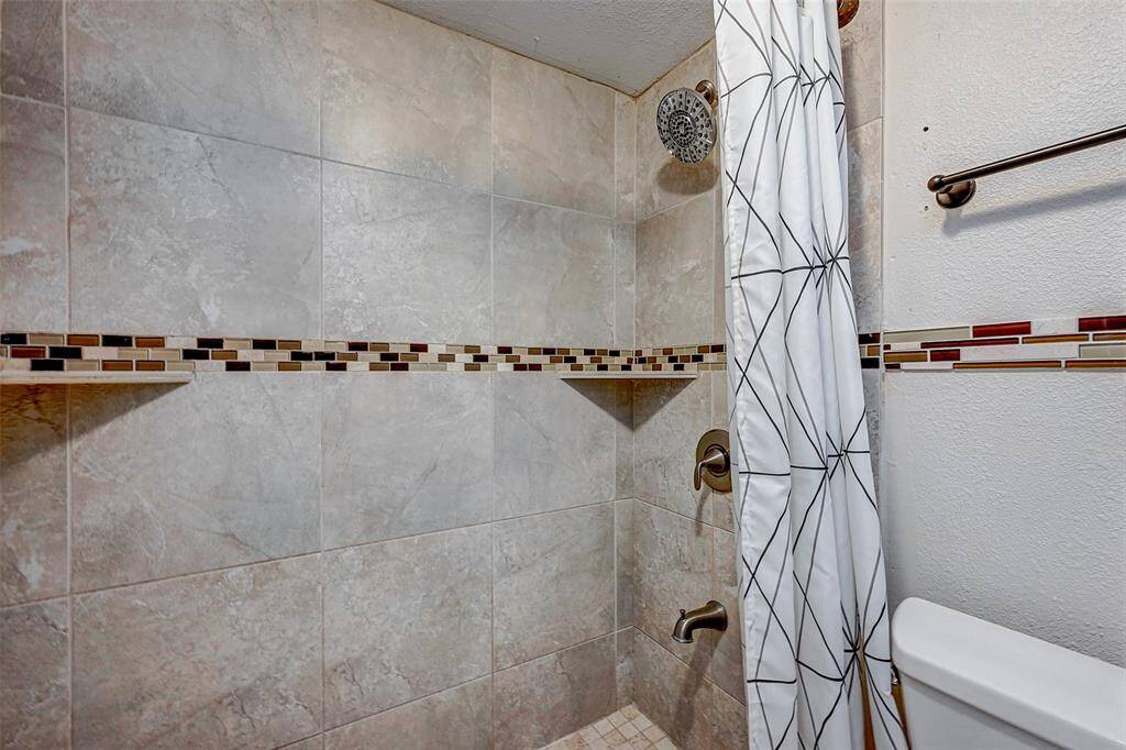 This bathroom features a tiled shower with a modern mosaic accent strip and a rainfall showerhead, offering a clean and contemporary look.