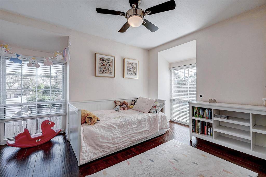 This cozy bedroom features built-in shelving, and large windows that let in plenty of natural light. The room is accented with a ceiling fan and dark wood flooring, providing a warm and inviting space perfect for children.