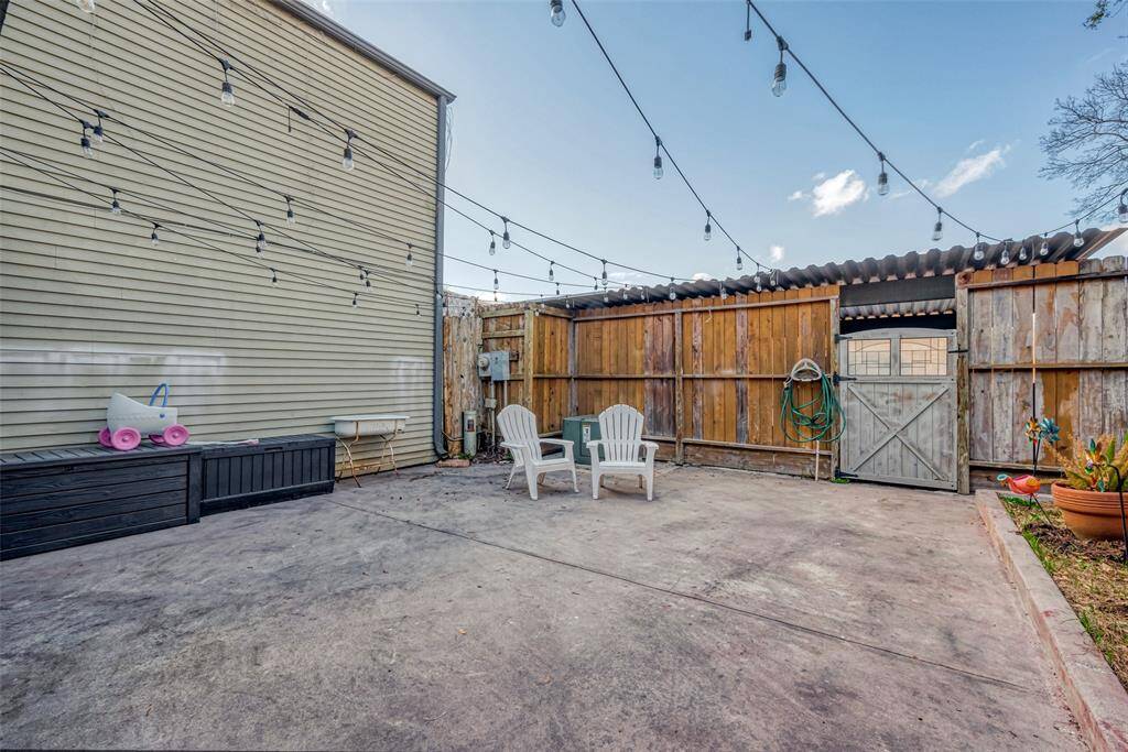 Cozy backyard patio with string lights overhead, fenced for privacy. Offering a charming outdoor space for relaxation.