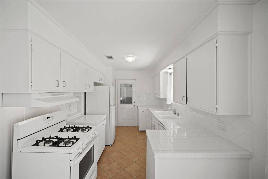 The Kitchen features Polished White Tile Countertops, Diagonally Set Polished White Tile Backsplash, and White Painted Cabinets and Drawers.  A Door, with Micro Mini Blind Inset, opens from the Kitchen to the Garage.