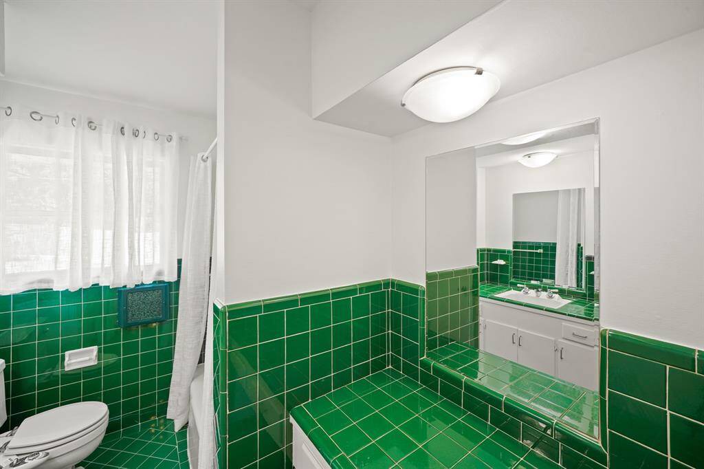 The Primary Bath features a Separate Vanity Area with Retro Emerald Green Tiled Counter, 2 Drawers, Beveled Mirror, and Flush Mount Light Fixture---Such Convenient Space!