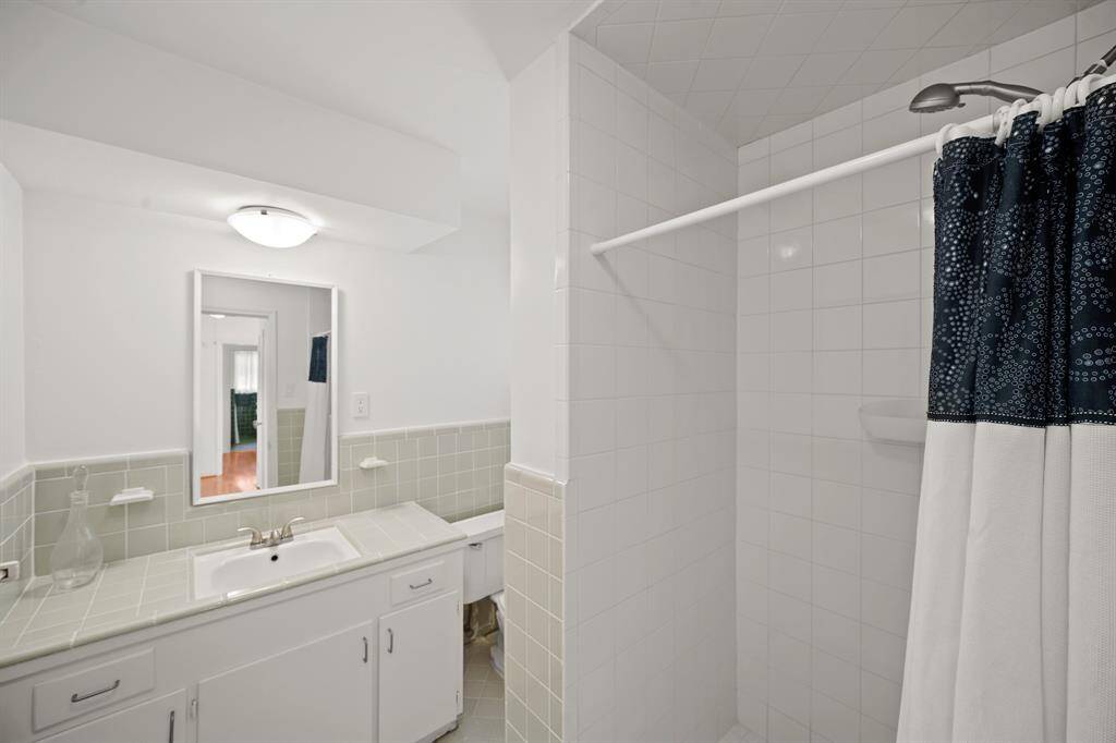 A Walk in Shower with White Tile Surround, Hand Held Shower Wand, and Built in Shampoo Shelves are featured in the Hall/Guest Bath.
