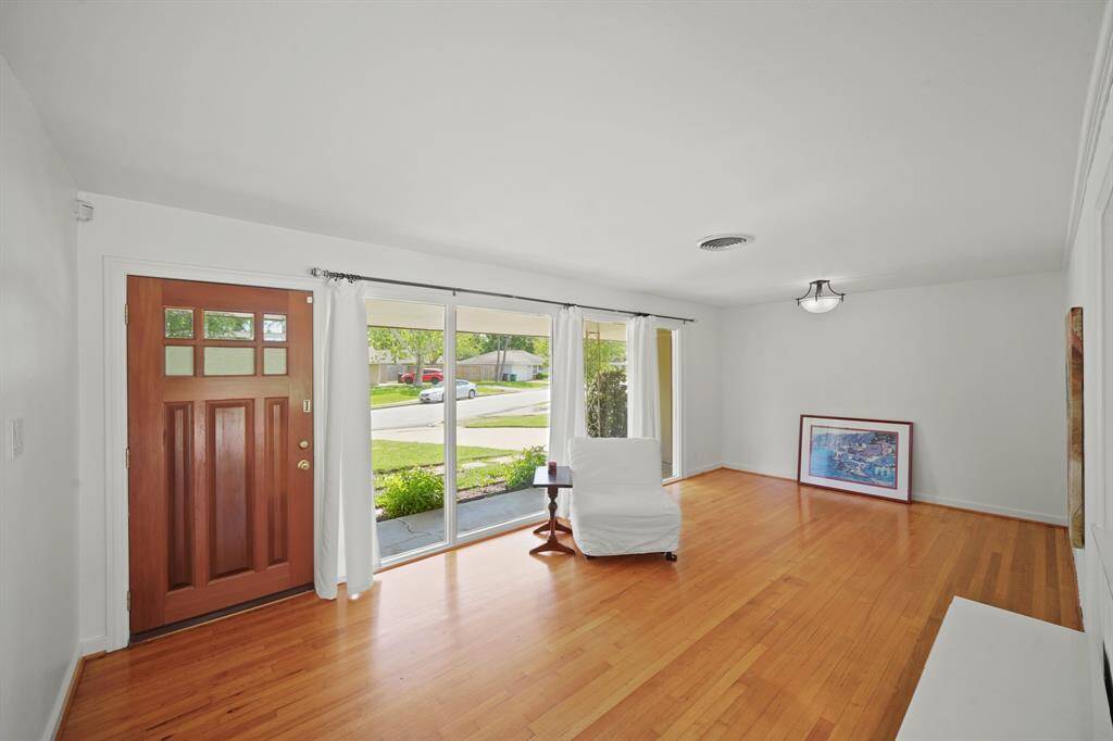 The Open and Bright Foyer features a Walnut Hued Front Door withBeveled Glass Inset, Oak Hardwood Floors, and Fresh White Designer Paint.