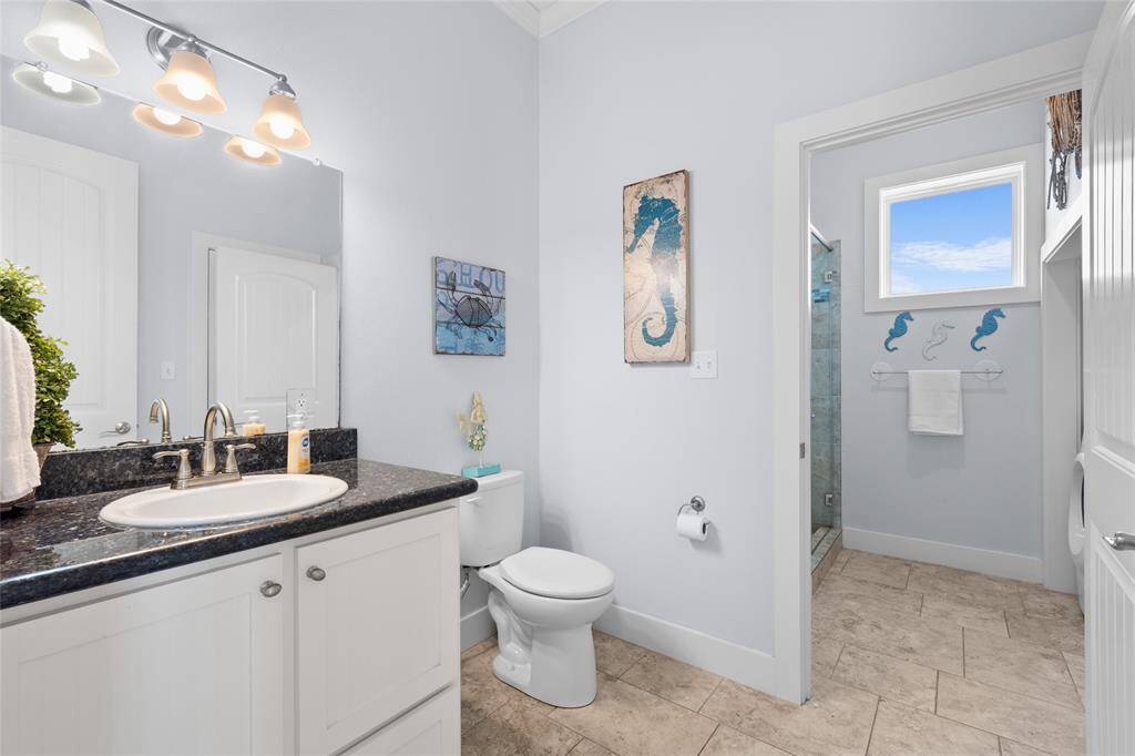This bathroom features a sleek design with light blue walls, a granite countertop, and modern fixtures. It includes a toilet, a shower with a glass door, and nautical-themed decor for a fresh, coastal vibe.