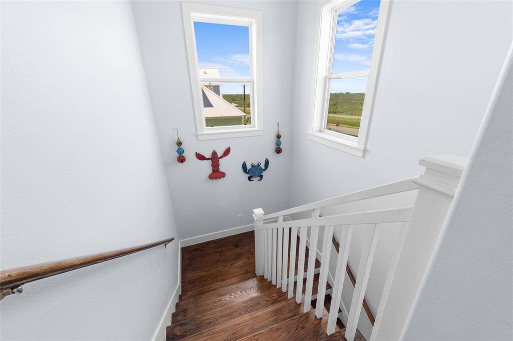 Bright staircase with wooden steps and white railing, featuring coastal-themed wall decor and two large windows offering scenic views.