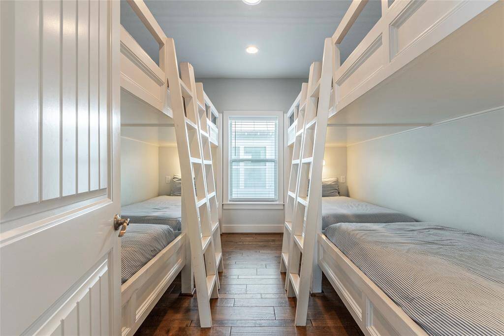 This cozy room features two sets of white bunk beds with ladders, ideal for maximizing space. The hardwood floors add warmth, and a window provides natural light, creating a bright and welcoming atmosphere. Perfect for a kids' room or guest space.