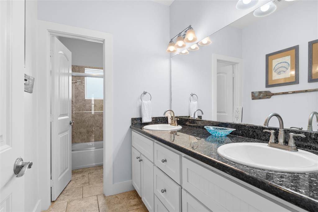This bathroom features a double vanity with granite countertops, modern fixtures, and ample cabinet space. It has a neutral color palette and a separate shower area with tiled walls, creating a clean and inviting atmosphere.