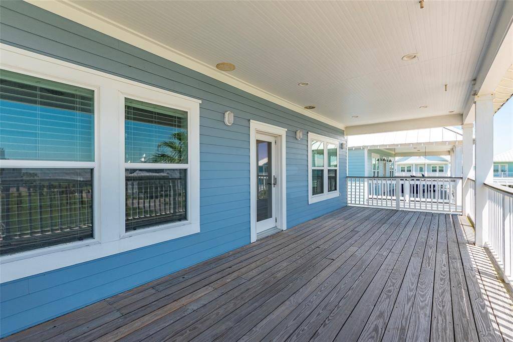 This photo showcases a spacious, covered wooden deck with a blue exterior, featuring multiple windows and a glass door. The area is ideal for enjoying outdoor relaxation and entertainment.