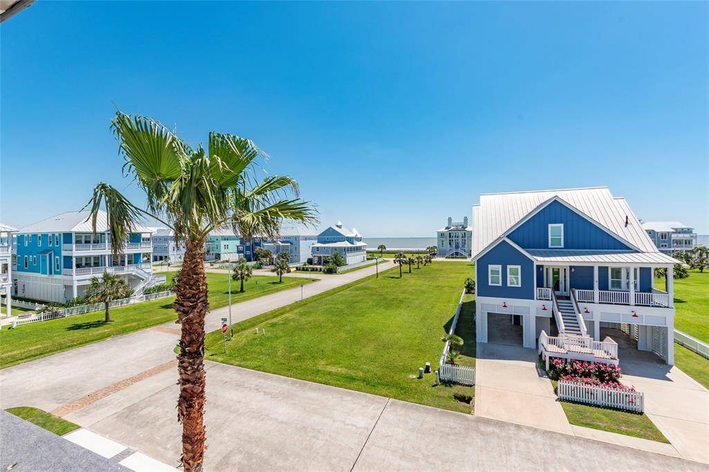 This photo showcases a coastal neighborhood with charming blue homes, palm trees, and a view of the water. The setting is open and sunny, offering a serene seaside ambiance.