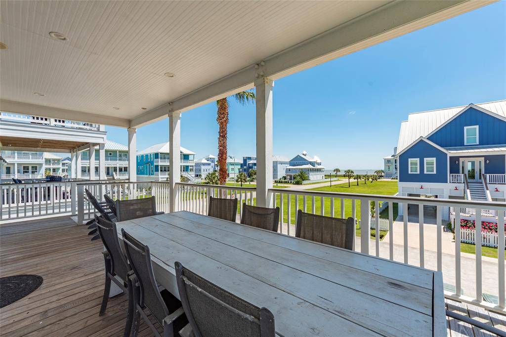 Spacious covered porch with a large dining table, offering a relaxing view of a well-maintained neighborhood and the ocean in the distance. Perfect for outdoor dining and enjoying coastal living.