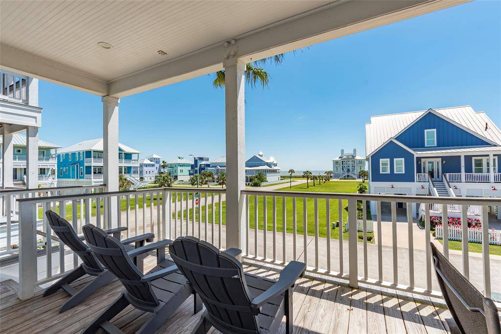 Charming coastal view from a spacious covered balcony with Adirondack chairs, overlooking a neighborhood of colorful beach houses and lush green lawns. Perfect for enjoying seaside living.
