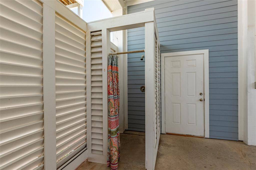 This photo shows an outdoor shower area with louvered privacy walls and a colorful curtain. It's adjacent to a blue siding wall and a white door, providing convenient access after outdoor activities.